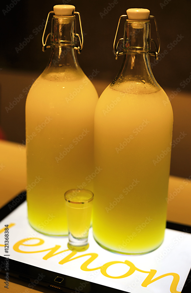 Lemoncello cocktail in two big bottles on table lighted by tablet underneath in cafe Lemoncello cocktail in two big bottles on table lighted by tablet underneath in cafe