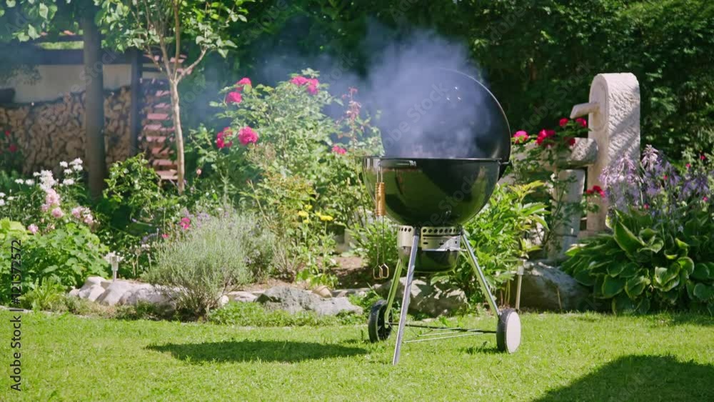 static shot of a smoking bbq kettle grill in the backyard