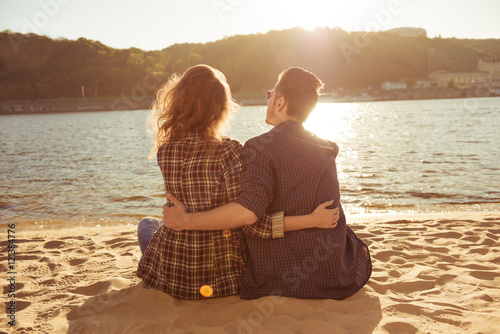 Back view of romantic couple sitting on the beach and huging