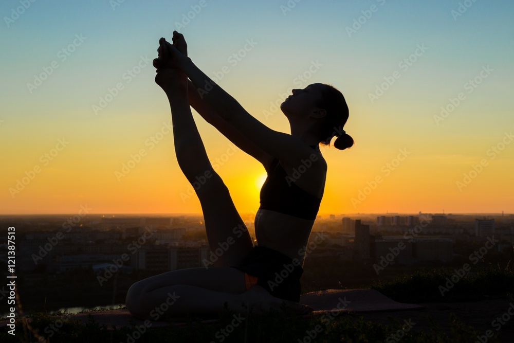 Silhouette of sporty woman doing yoga in floating boat pose in the park ...