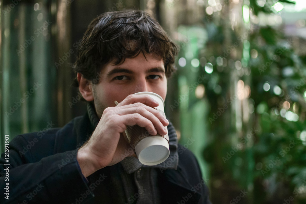 Young handsome man in coat drinking coffee looking at camera Young handsome man in coat drinking coffee looking at camera