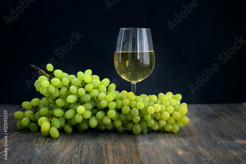 Bunch of grapes on wooden table with white wine in wineglass. Special light, selective focus.