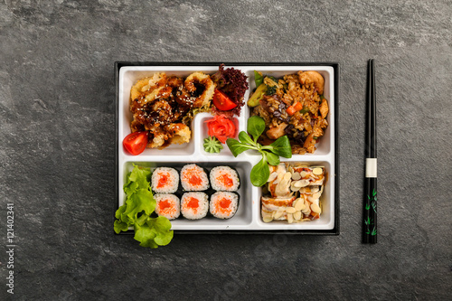 Traditional Japanese Bento lunch business. As part of the rice, sushi, vegetables, fish. Packaging is on a black background, next to chopsticks. 