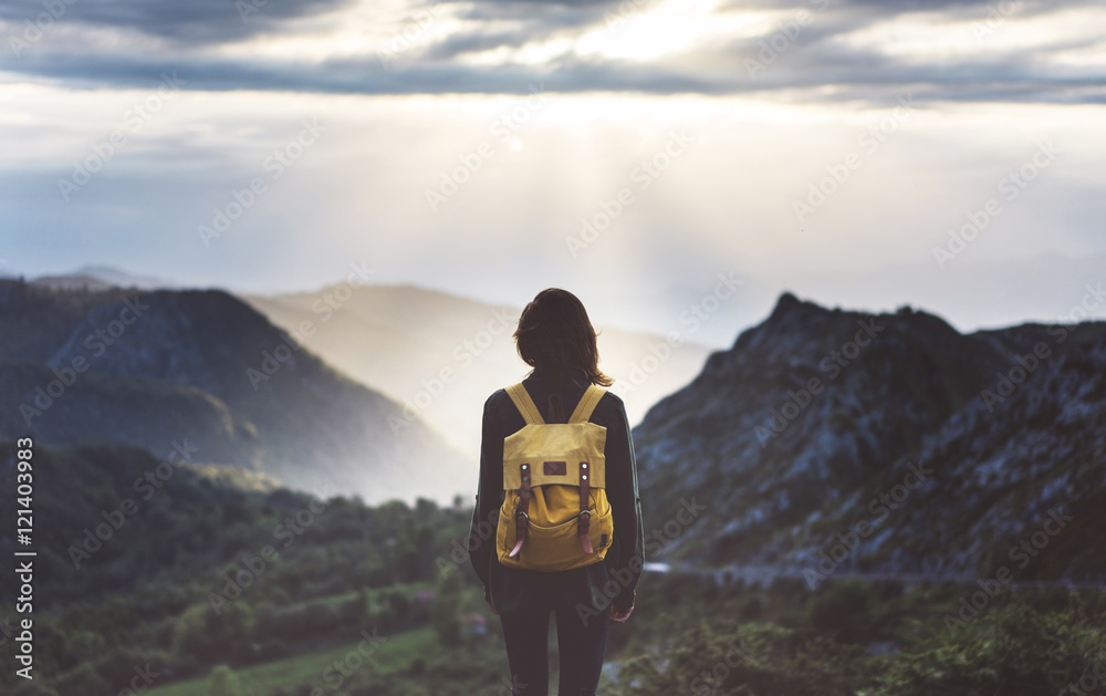 Hipster young girl with bright backpack enjoying sunset on peak of foggy mountain. Tourist traveler on background valley landscape view mockup. Hiker looking sunlight flare in trip Picos de Europa - obrazy, fototapety, plakaty 