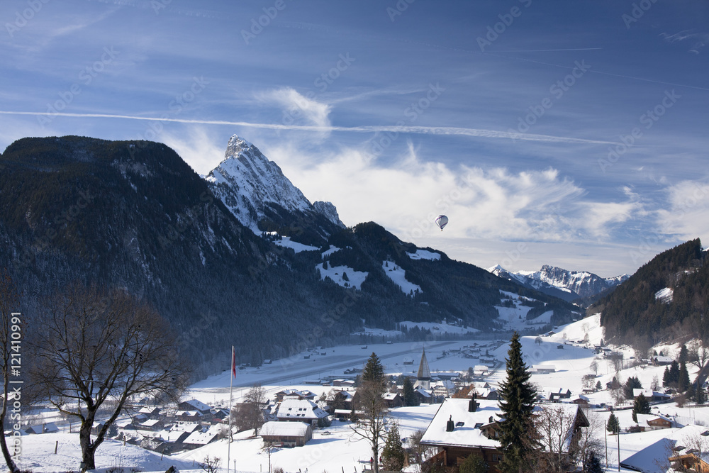 Landscape of Gstaad in Switzerland, with snow in winter, with a with a hot-air balloon in the blue sky