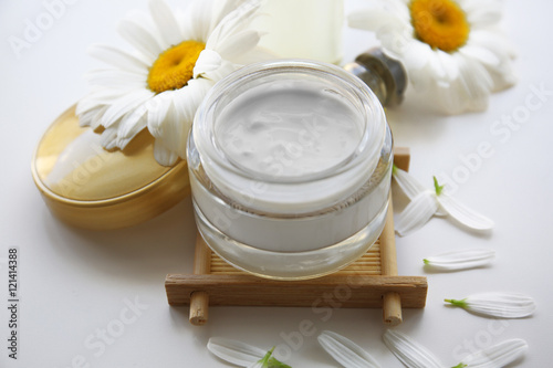 Cosmetic cream and chamomile flowers on white background