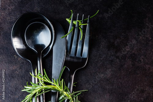 Set of cutlery knife, spoon, fork, rosemary. Black background.