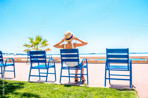 Woman sitting on the blue chairs of the promenade in Cannes city. This chairs are iconic symbol and tourist attraction of Cannes in France