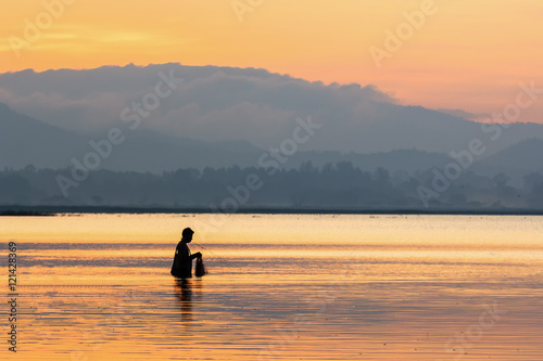 Siluate fishermen in action when fishing in the lake with sunrise , Thailand