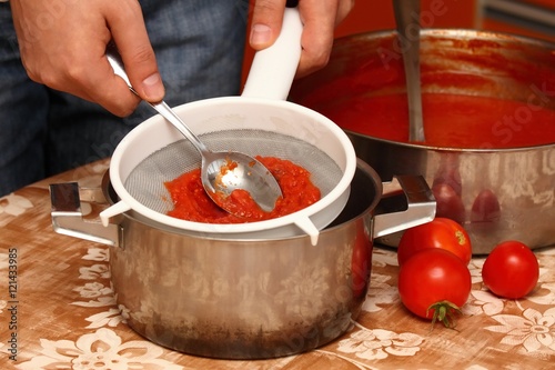 Foto Man making ketchup, tomatoes boiled to mush pressed through strainer
