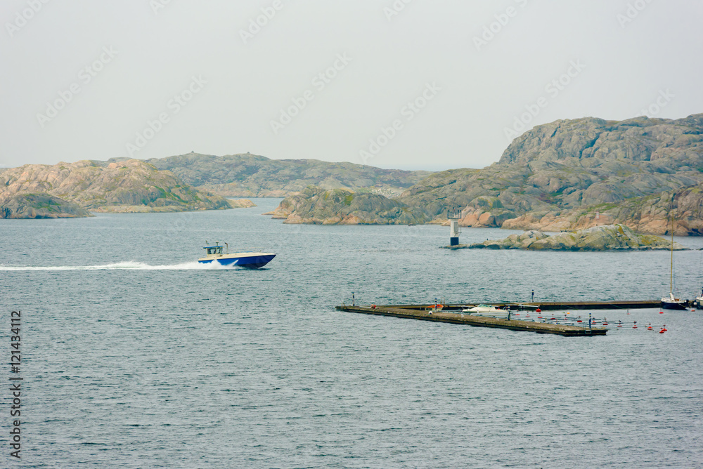 Obraz premium Blue motorboat speeding to the marina with rocky islets in background one misty morning in fall. The Swedish west coast near Skarhamn on Tjorn.