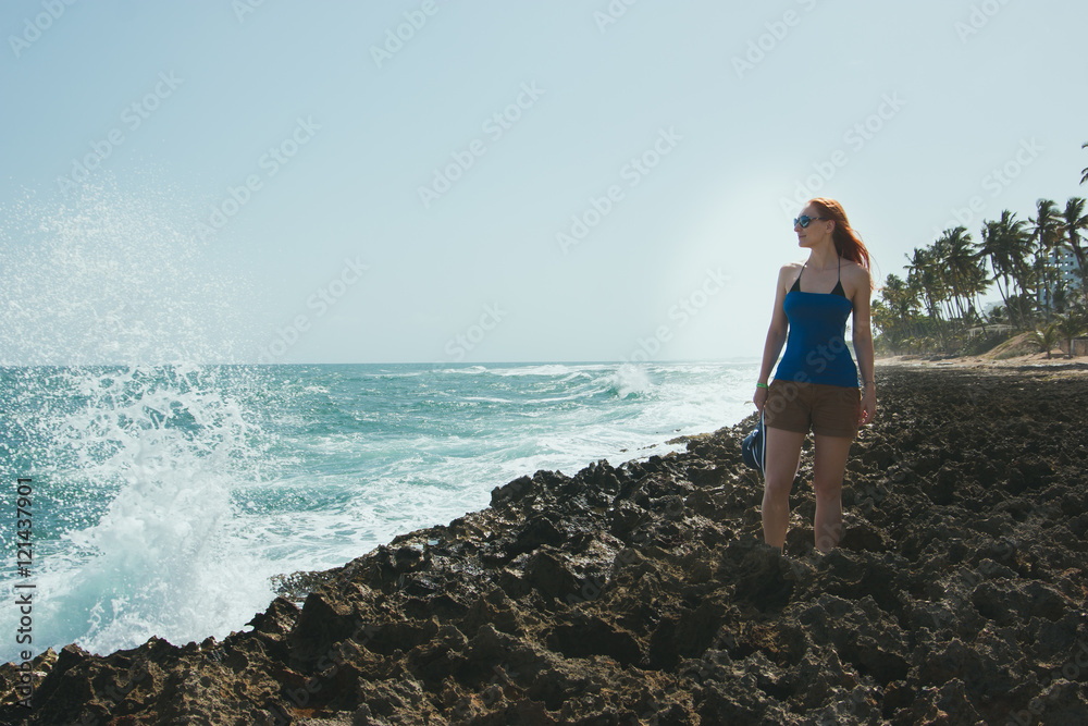 Young woman in in shorts and t-shirt standing on rocks  looking to a sea