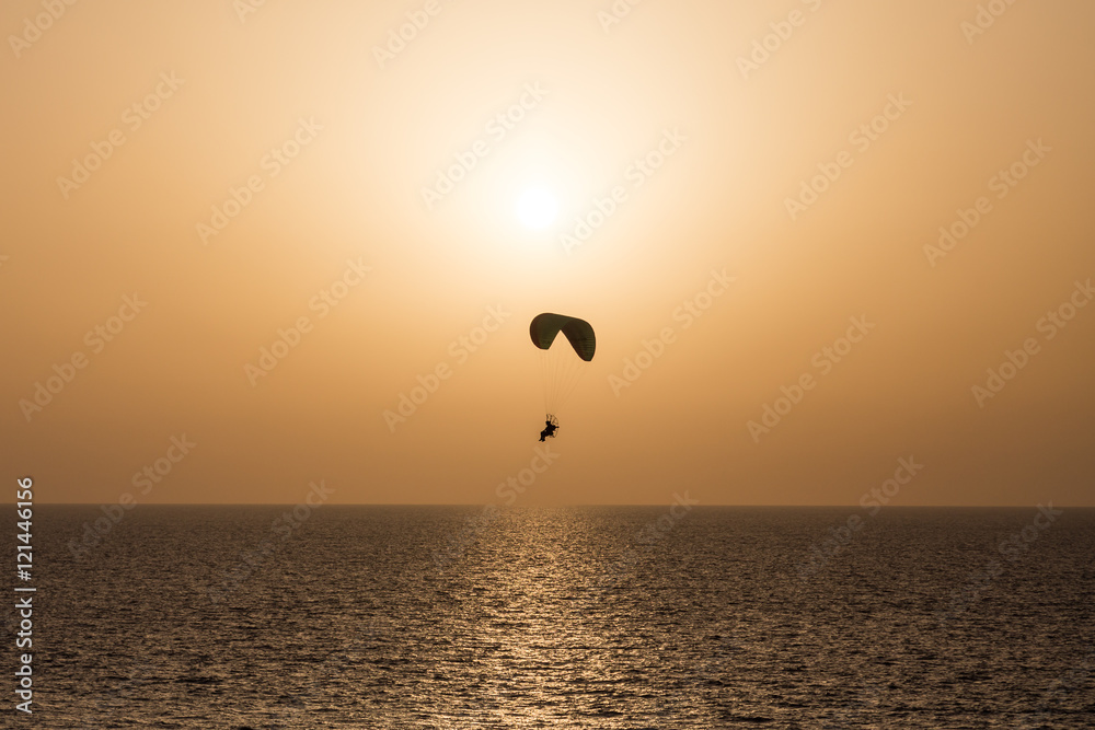 Silhouette of a Propelled Paraglider on a clear sunset sky above the sea Silhouette of a Propelled Paraglider on a clear sunset sky above the sea