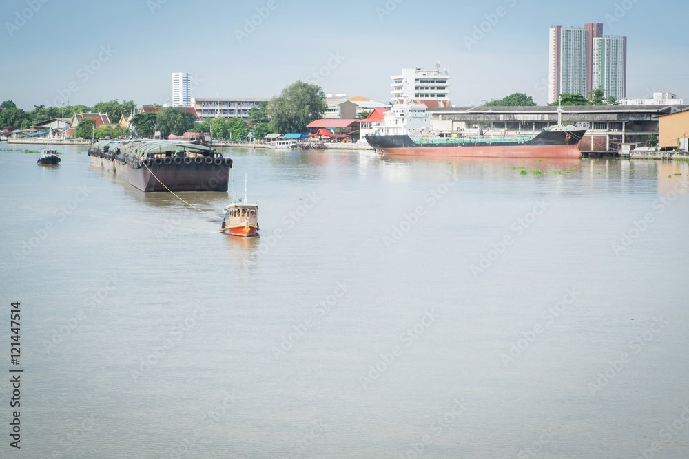 A small tug boat towing a large sand tanker in the Chao Phraya River, bangkok, thailand.