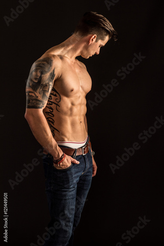 Tätowierter muskulöser Mann mit freiem Oberkörper schaut sinnlich - Junger Mann mit Sixpack auf schwarzem Hintergrund