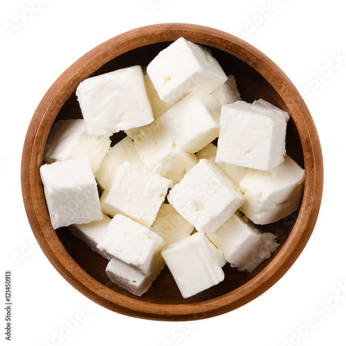 Greek Feta cheese cubes in a wooden bowl on white background. Cubes of a brined curd white cheese made in Greece from milk of sheeps and goats. Crumbly aged cheese with slightly grainy texture.
