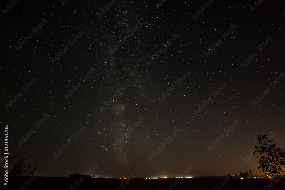 Fototapeta premium Bright stars in the night sky above the city with street lightin