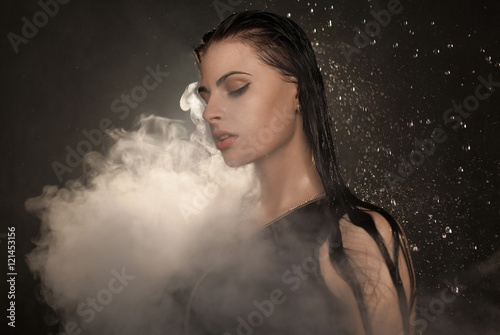 Young beautiful woman vaping e-cigarette. Water flowing on lwoman face. photo