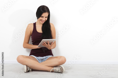 Happy young woman sitting on floor with crossed legs and using tablet on white background