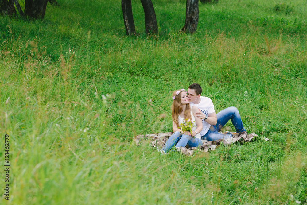 A view of a couple in a green forest area cuddling on a plaid lovely