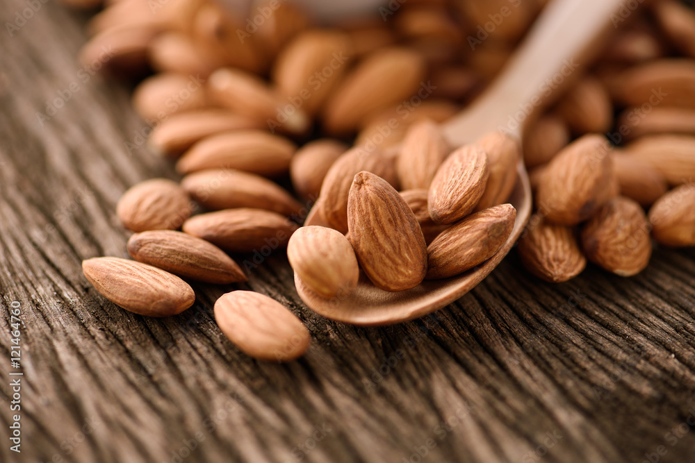 close up of almonds in a wood spoon on grained wood background close up of almonds in a wood spoon on grained wood background