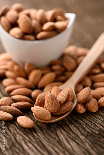 almonds in a white ceramic bowl with wood spoon on grained wood