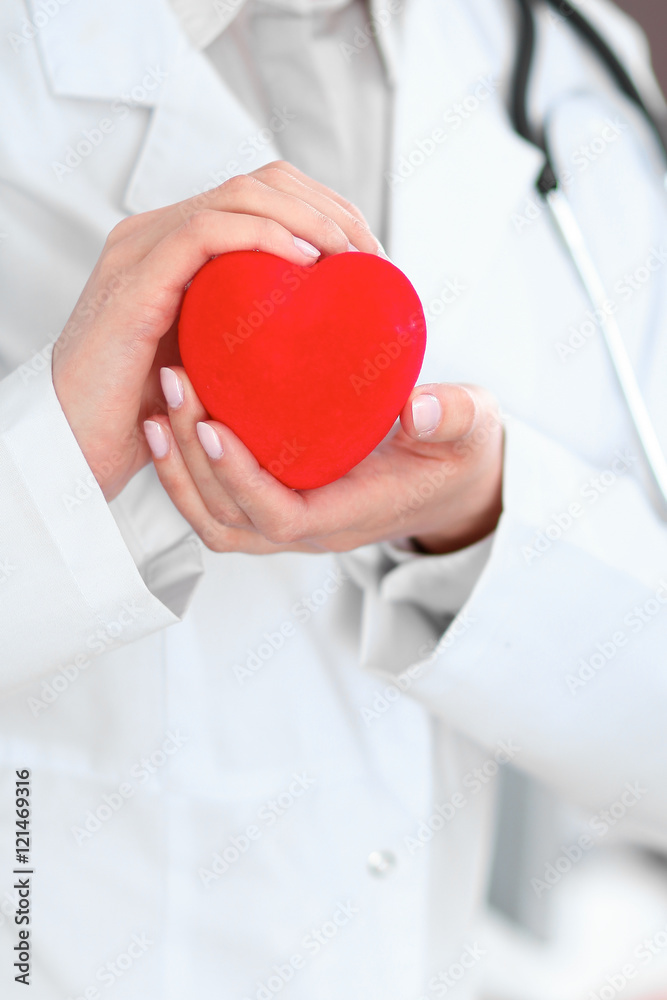Female doctor with stethoscope holding heart. Patients couple sitting in the background Female doctor with stethoscope holding heart. Patients couple sitting in the background