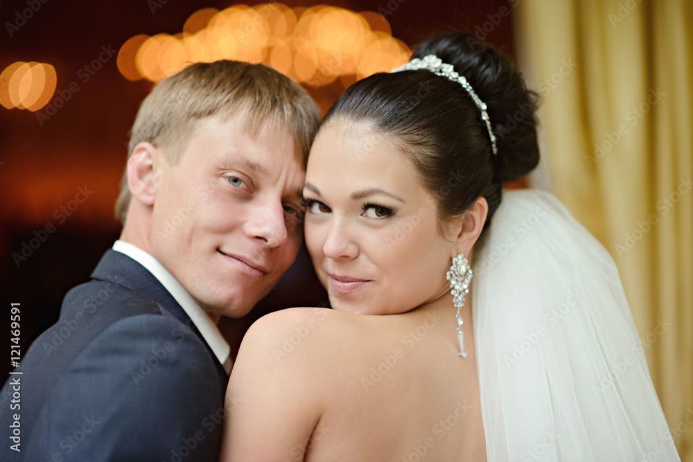 Wedding couple indoors is hugging each other. Beautiful model girl in white dress. Man in suit. Beauty bride with groom. Female and male portrait. Woman with lace veil. Cute lady and handsome guy