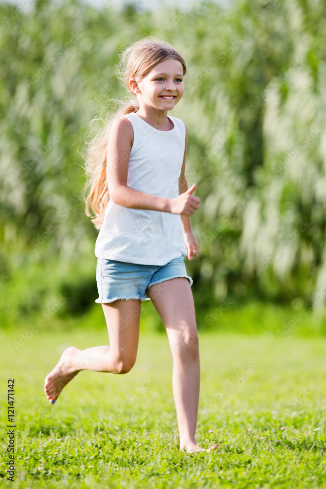 Glad girl in elementary school age running on grass