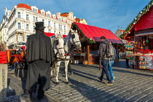 Photography Coachman in a black hat and coat and white horses hitched to horse carriage waiting for tourists on Christmas Old Town Square of Prague, Czech Republic