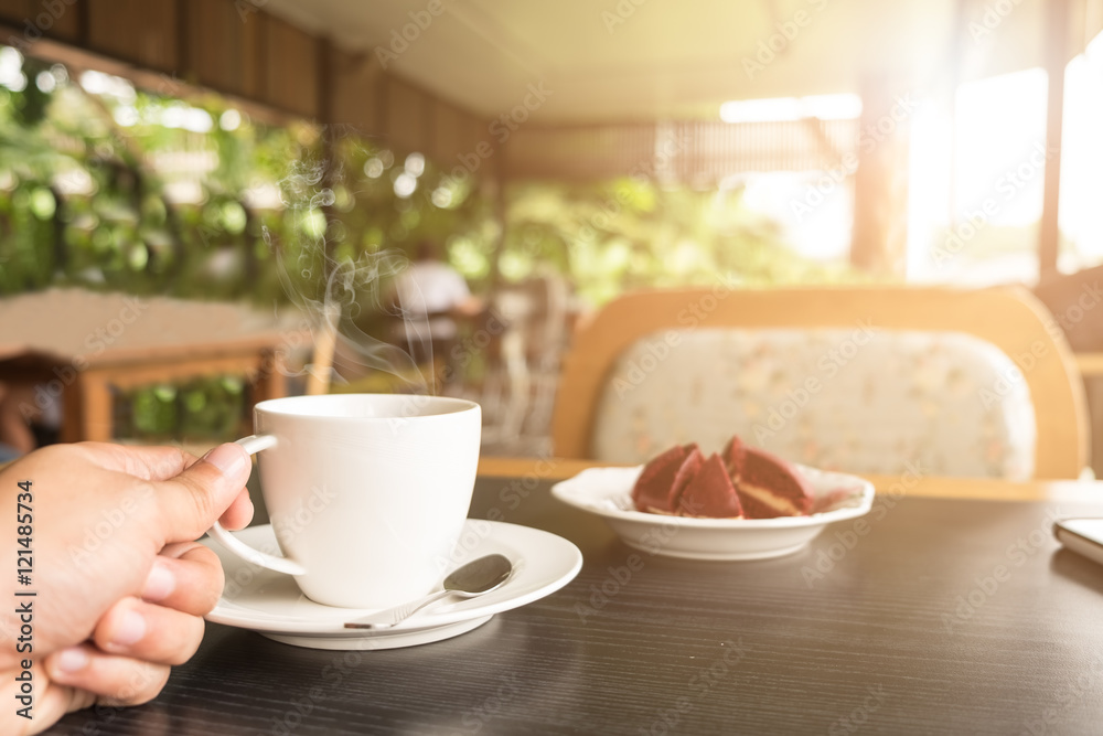 Sunrise Monring with hand holding a coffee cup with red cake at coffee shop