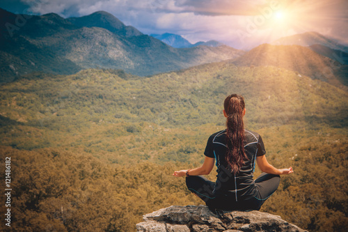 Young woman sits at peak of mountain in lotus pose, doing yoga and feel harmony of body and nature. Relax and meditation on outdoor.