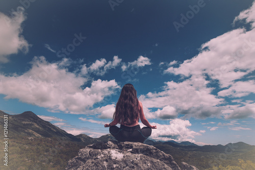 Woman sits at peak of mountain in lotus pose, doing yoga and feel harmony of body and nature. Relax and meditation on outdoor. 