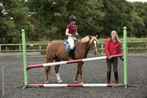 Erecting a jump in an outdoor riding school - September 2016 - Riding instructor lifting a pole to increase the height of the fence for the pupil riding a Chestnut pony