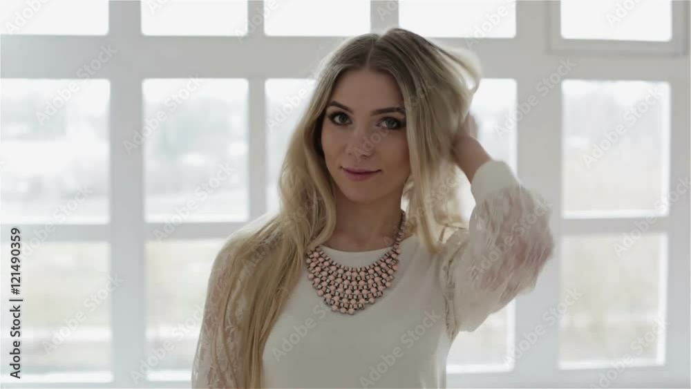 A beautiful blonde girl is standing against the large window and showing herself. A beautiful blonde girl is standing against the large window and showing herself.