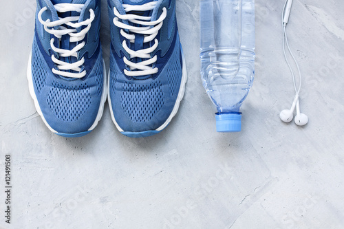 Flat lay sport shoes, bottle of water and earphones on gray conc