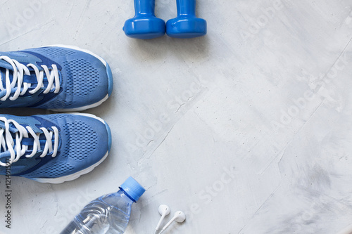 Flat lay sport shoes, bottle of water, dumbbells and earphones o