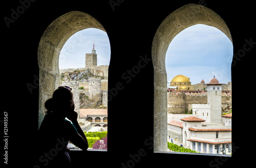 A silhouette of a girl standing in the shade and looks out the window at the old castle town. Georgia, castle Rabat
