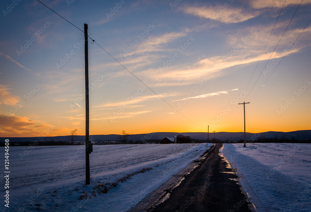 Sunset over a country road through snow covered fields in rural
