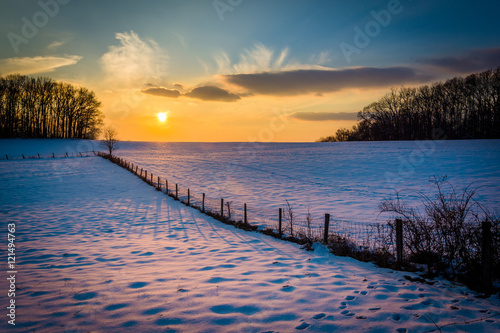 Winter sunset over a fence and snow covered farm field in rural