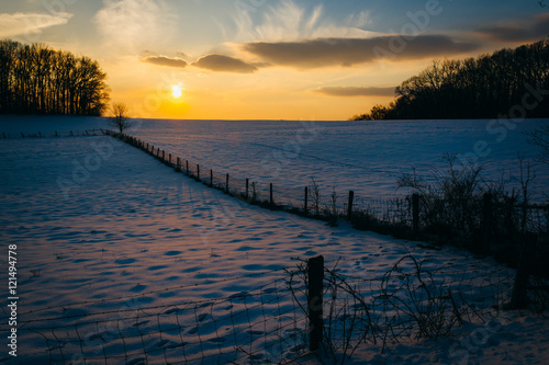 Winter sunset over a fence and snow covered farm field in rural