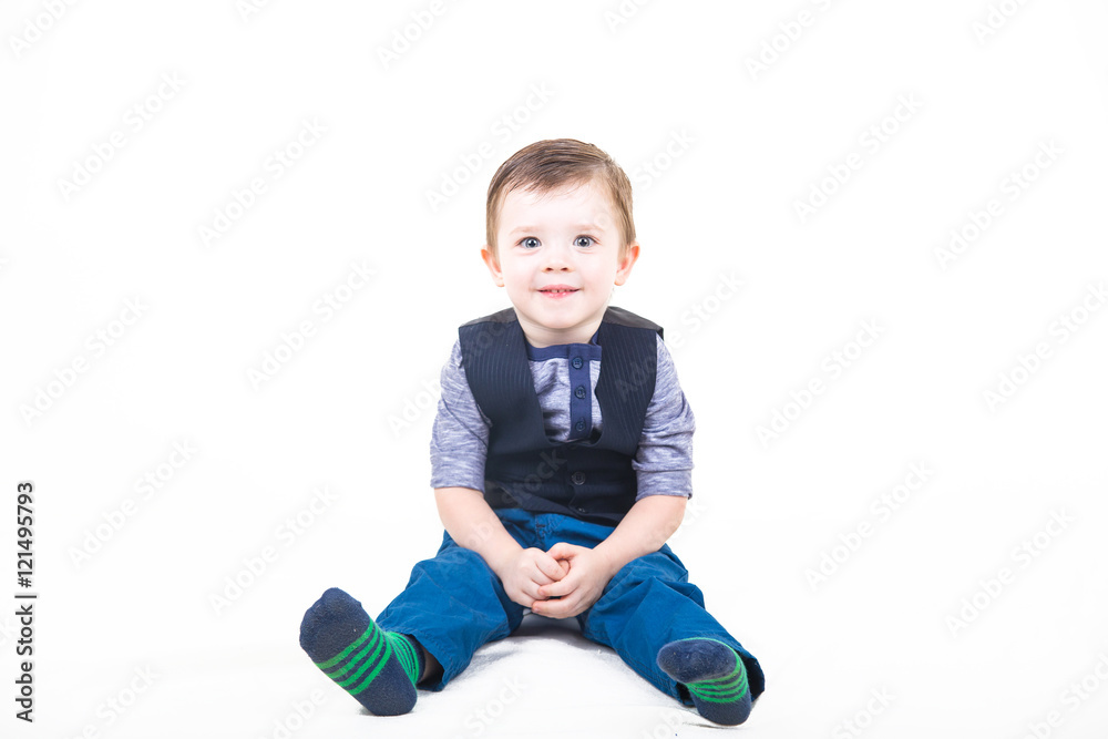 Cute kid in a striped knitted socks, blue jeans and a batch file with a vest sits isolated on a white background Cute kid in a striped knitted socks, blue jeans and a batch file with a vest sits isolated on a white background