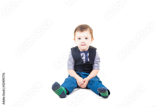 Cute kid in a striped knitted socks, blue jeans and a batch file with a vest sits isolated on a white background