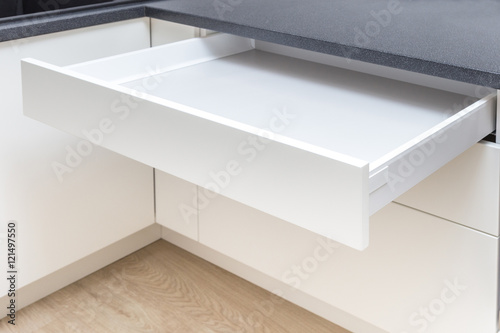 Opened white drawer in a kitchen cabinet with an handleless front, tip to open system 