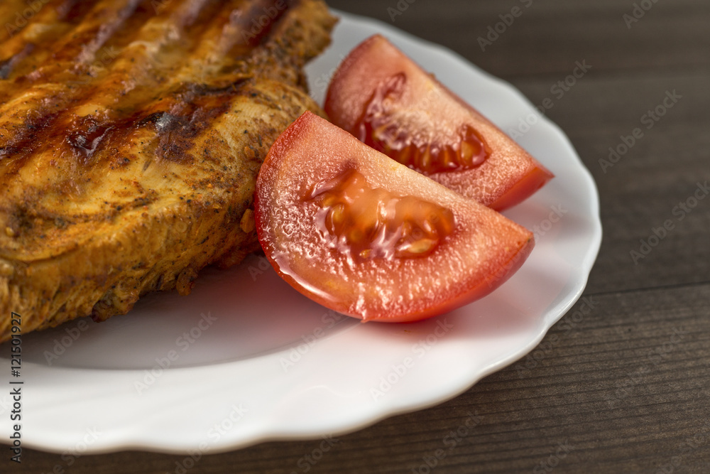 Fototapeta premium grilled chicken breast with tomatoes served on white plate on wooden table