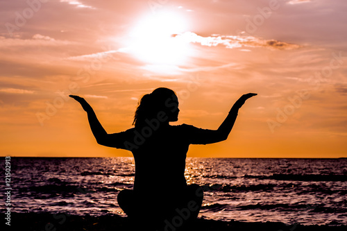 Female yoga lotos silhouette on beautiful beach during sunset. © eplisterra