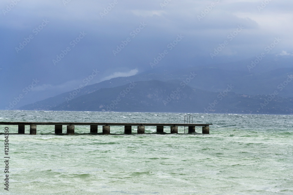 Obraz premium Wooden pier with waves on Lago di Garda, Sirmione, Italy