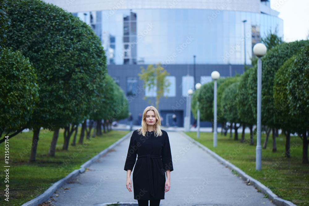 Blonde girl is in a Park with trees in the background of the building with a glass facade Blonde girl is in a Park with trees in the background of the building with a glass facade