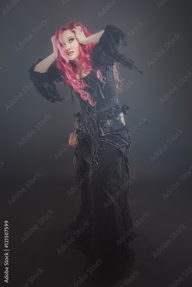 Attractive woman with red hair in witches costume, in the fog, clutching her head