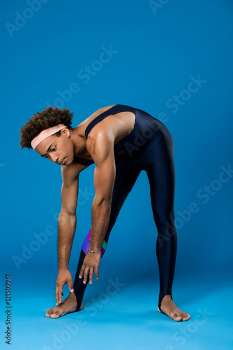 Sportive african man stretching, warming up over blue background.